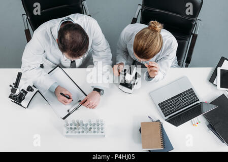 overhead view of scientific researchers in white coats working together at workplace in laboratory