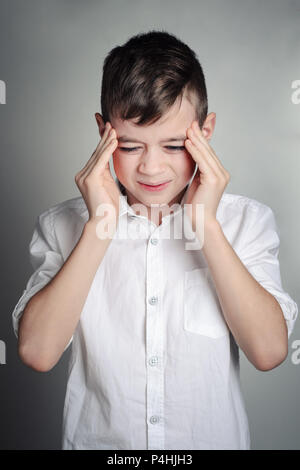 a boy in a white shirt suffers from a headache, holds his hands at his temple, a painful expression on his face. Studio portrait Stock Photo
