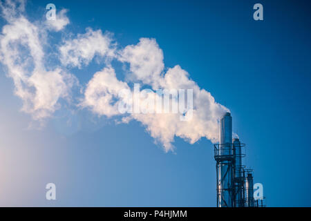 three chimneys smoking white smoke in a row against a blue sky in the sun. The concept of environmental pollution Stock Photo