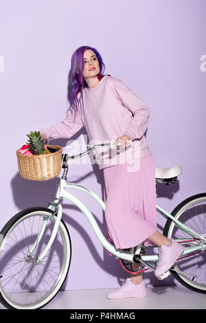 attractive woman in pink clothing on bicycle with pineapple and bananas in basket Stock Photo