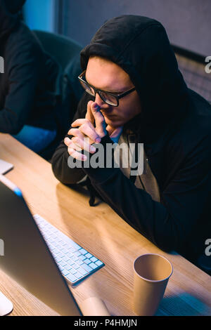 thoughtful hooded hacker looking at computer screen Stock Photo