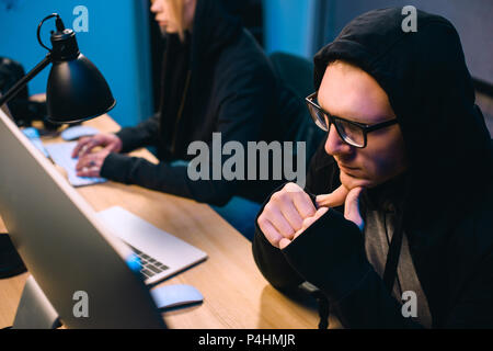 thoughtful young hacker looking at computer screen in dark room Stock Photo