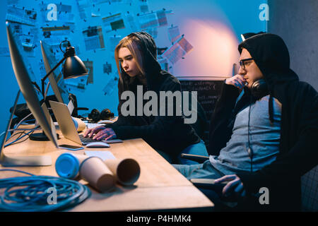 couple of young hackers using laptop at workplace in dark room Stock Photo