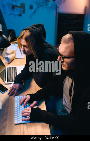 confident couple of hackers working on malware together in dark room Stock Photo