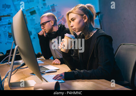 young female hacker drinking coffee and working on malware with accomplice Stock Photo