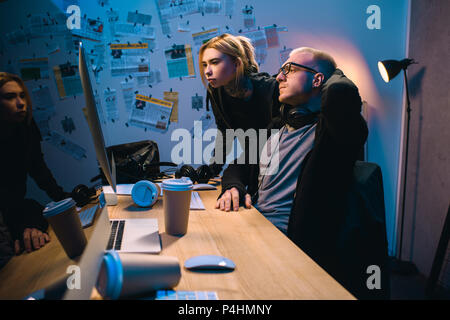 couple of hackers looking at computer screen together in dark room Stock Photo