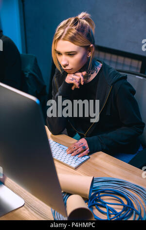 young thoughtful female hacker looking at computer screen Stock Photo
