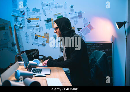 side view of hooded young hacker working with computer Stock Photo