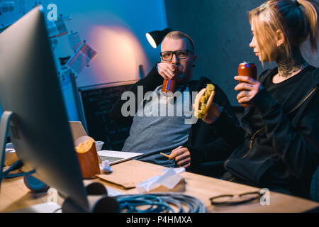 young hackers drinking beer and eating junk food while working on malware Stock Photo