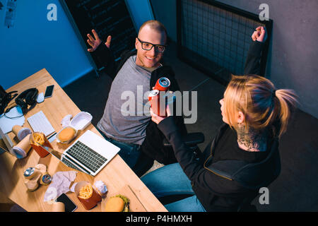 high angle view of celebrating couple of hackers clinking cans of beer at workplace Stock Photo