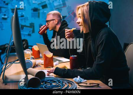 side view of hackers eating junk food while working on malware Stock Photo