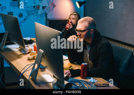 hackers drinking beer and eating junk food while working on malware Stock Photo