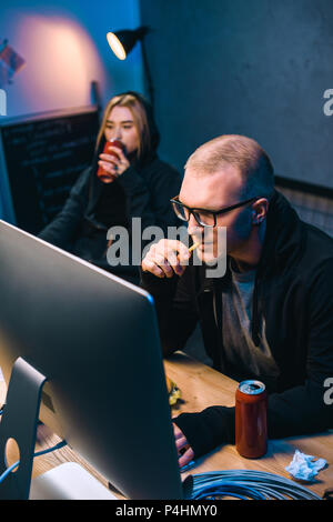 young hackers drinking beer and eating junk food while working on malware Stock Photo