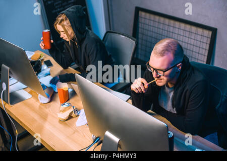 couple of hackers drinking beer and eating junk food while working on malware Stock Photo