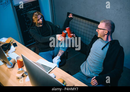 high angle view of couple of hackers clinking cans of beer at workplace Stock Photo