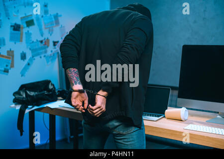 rear view of handcuffed hacker in front of his work desk Stock Photo