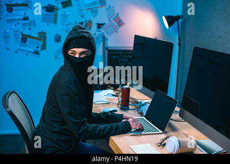 female hacker in mask developing malware at workplace Stock Photo
