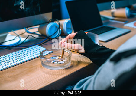 cropped shot of hacker putting cigarette into ashtray Stock Photo