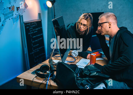 thoughtful couple of hackers looking at computer screen together in dark room Stock Photo
