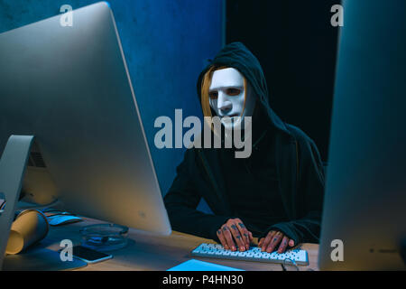 masked female hacker developing malware in dark room Stock Photo