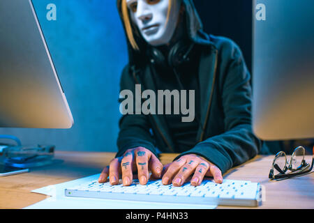 close-up shot of masked female hacker with tattoos on hands developing malware Stock Photo
