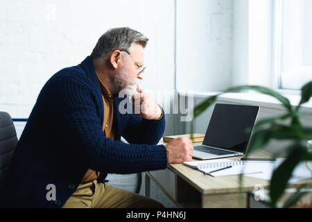 side view of focused senior man in eyeglasses using laptop with blank screen Stock Photo