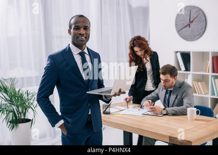Young african businessman with laptop and two colleagues doing paperwork at table Stock Photo