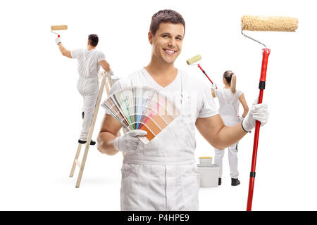 Painter holding a color swatch and a paint roller with two painters painting behind him isolated on white background Stock Photo