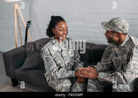African american man and woman soldiers holding hands while sitting on sofa Stock Photo