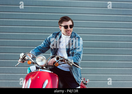 happy young man in denim jacket on vintage red scooter looking away Stock Photo