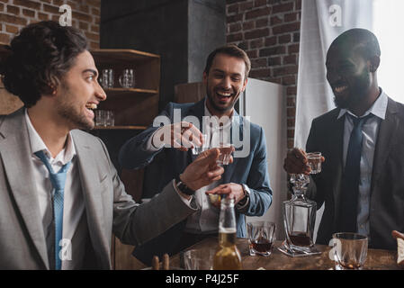 smiling multiethnic male friends in suits drinking tequila together Stock Photo