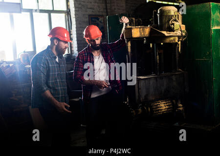 carpenters in protective helmets using machine tool at sawmill Stock Photo