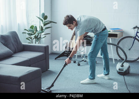 male teenager cleaning floor near sofa with vacuum cleaner Stock Photo