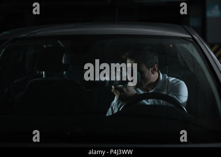 male private detective spying by camera with object glass from his car Stock Photo