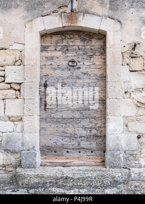 very old thick wooden medieval door in ancient limestone wall Stock Photo