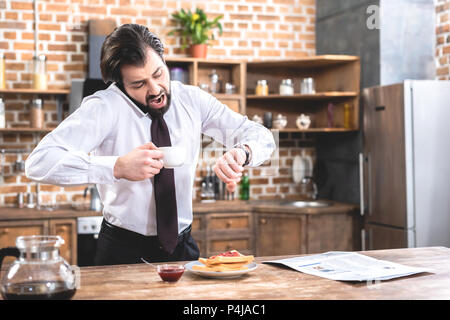 shocked handsome loner businessman talking by smartphone and checking time at kitchen Stock Photo