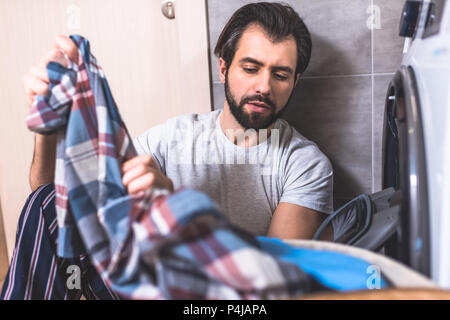handsome loner taking clothes for washing near washing machine in bathroom Stock Photo
