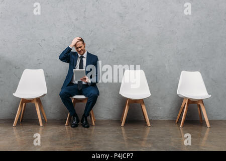 young frustrated businessman sitting on chair with tablet Stock Photo