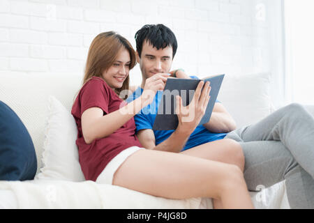 Spending nice time at home. Beautiful young loving couple reading book and smiling at couch in living room at home. Stock Photo