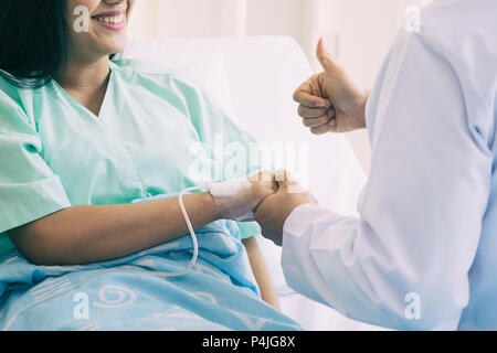 Hand of man doctor reassuring his female patient with thump up in bed at hospital. Medical ethics and trust concept. Stock Photo