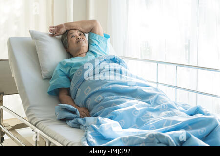 Asian depressed elderly woman patients lying on bed looking out the window in hospital. Elderly woman patients is glad recovered from the illness. Stock Photo