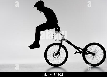 silhouette of trial biker performing stunt on bicycle on white Stock Photo