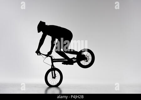 silhouette of trial cyclist performing front wheel stand on white Stock Photo