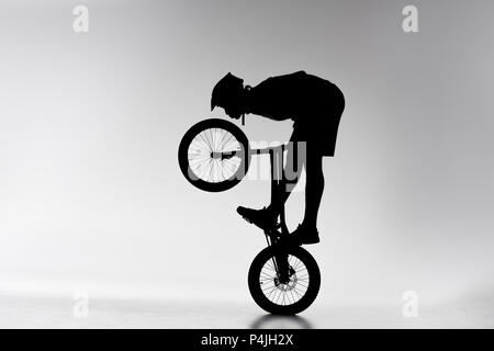 silhouette of trial biker performing balancing stunt on bicycle on white Stock Photo