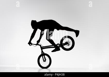 silhouette of trial biker performing front wheel balancing stunt on bicycle on white Stock Photo