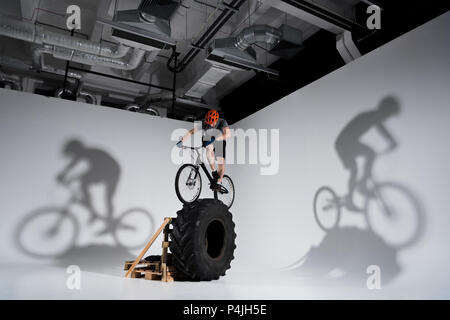 young athletic trial biker balancing on tractor wheel Stock Photo