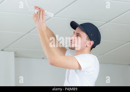 handsome young builder installing light bulb indoors Stock Photo
