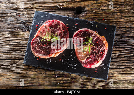 Two pieces raw beef shank on slate board and wooden table.. Stock Photo