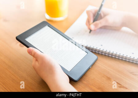 Girl is reading ebook on digital tablet device and is taking notes Stock Photo