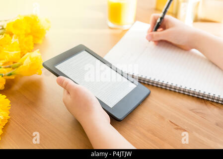 Girl is reading ebook on digital tablet device and is taking notes Stock Photo
